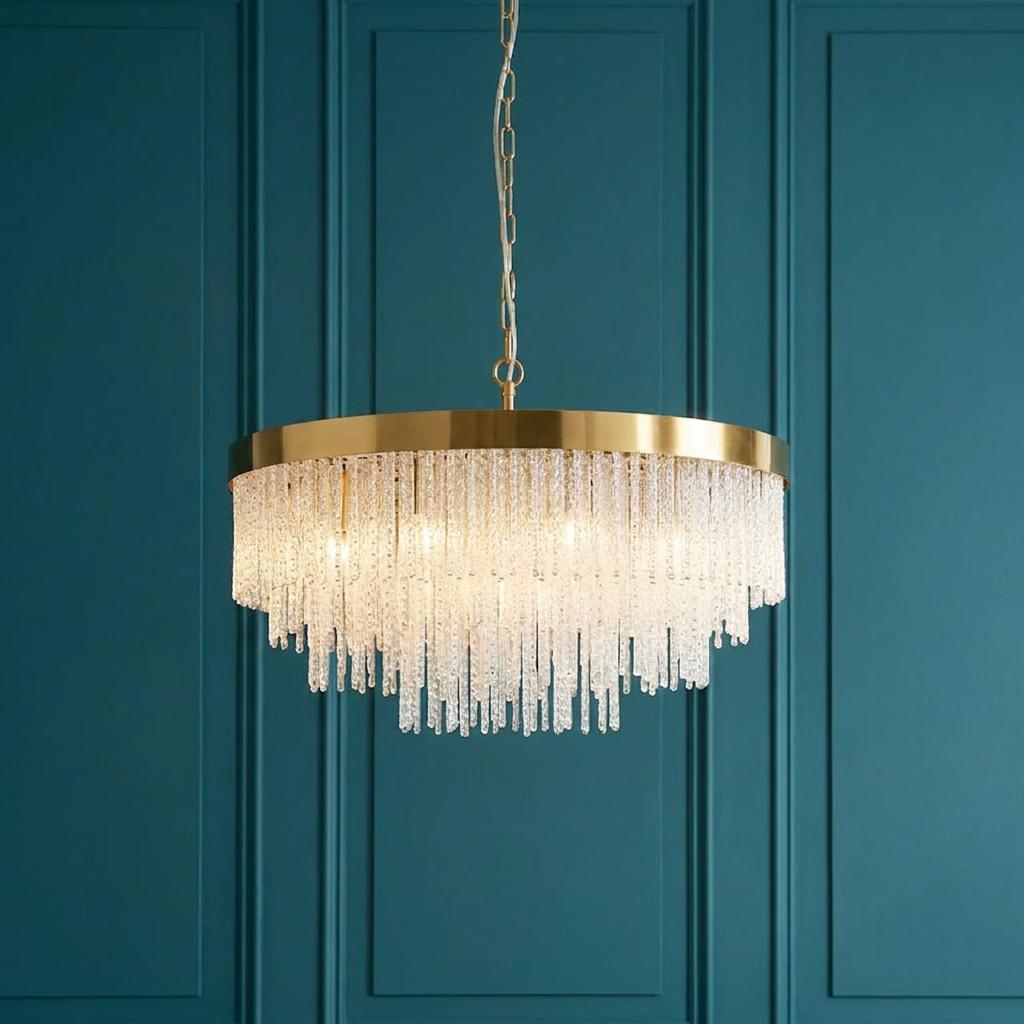 Anistoria Grand brass pendant light with tiered glass rods hanging against a teal paneled wall.