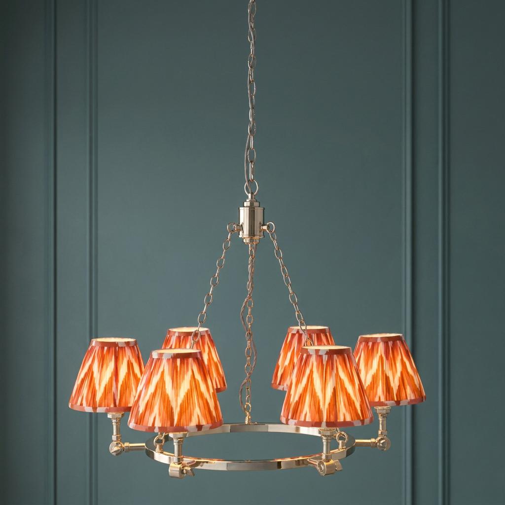 Five-light nickel chandelier with orange and white zigzag shades, hanging against a dark green paneled wall.