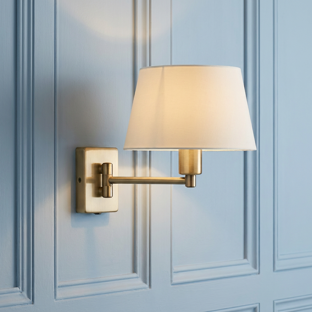 Antique brass single swing arm wall light with a white shade mounted on a light blue paneled wall.