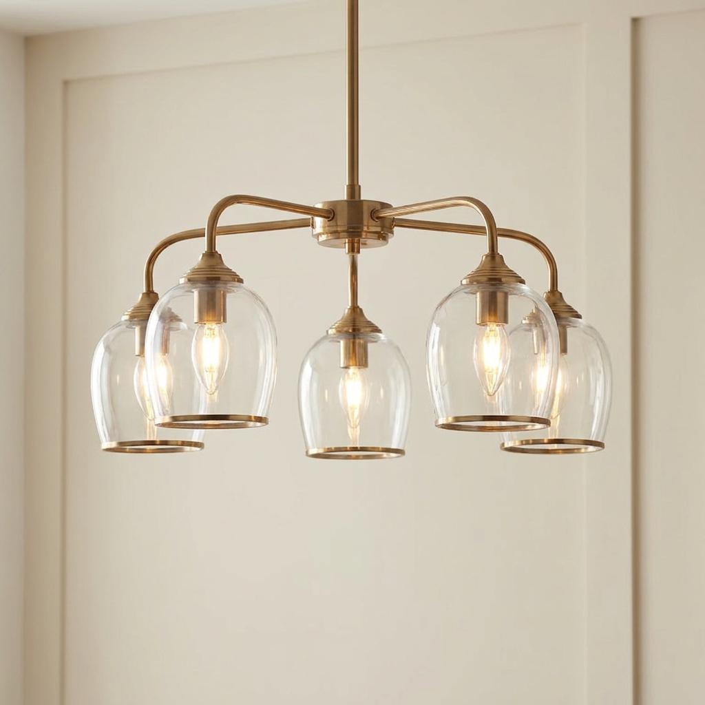 Modern 5-light brass pendant chandelier featuring clear glass shades and warm lit bulbs against a neutral wall.
