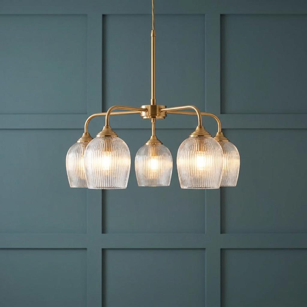 Brass 5-light pendant with ribbed glass shades hanging against a teal paneled wall.