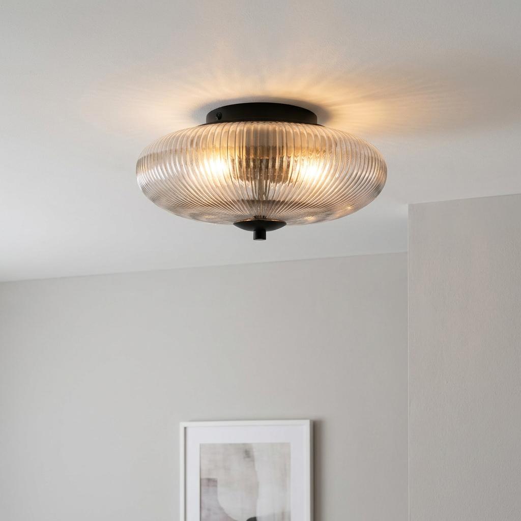 Elliptical ribbed glass ceiling light with black hardware emitting a warm glow in a neutral room.
