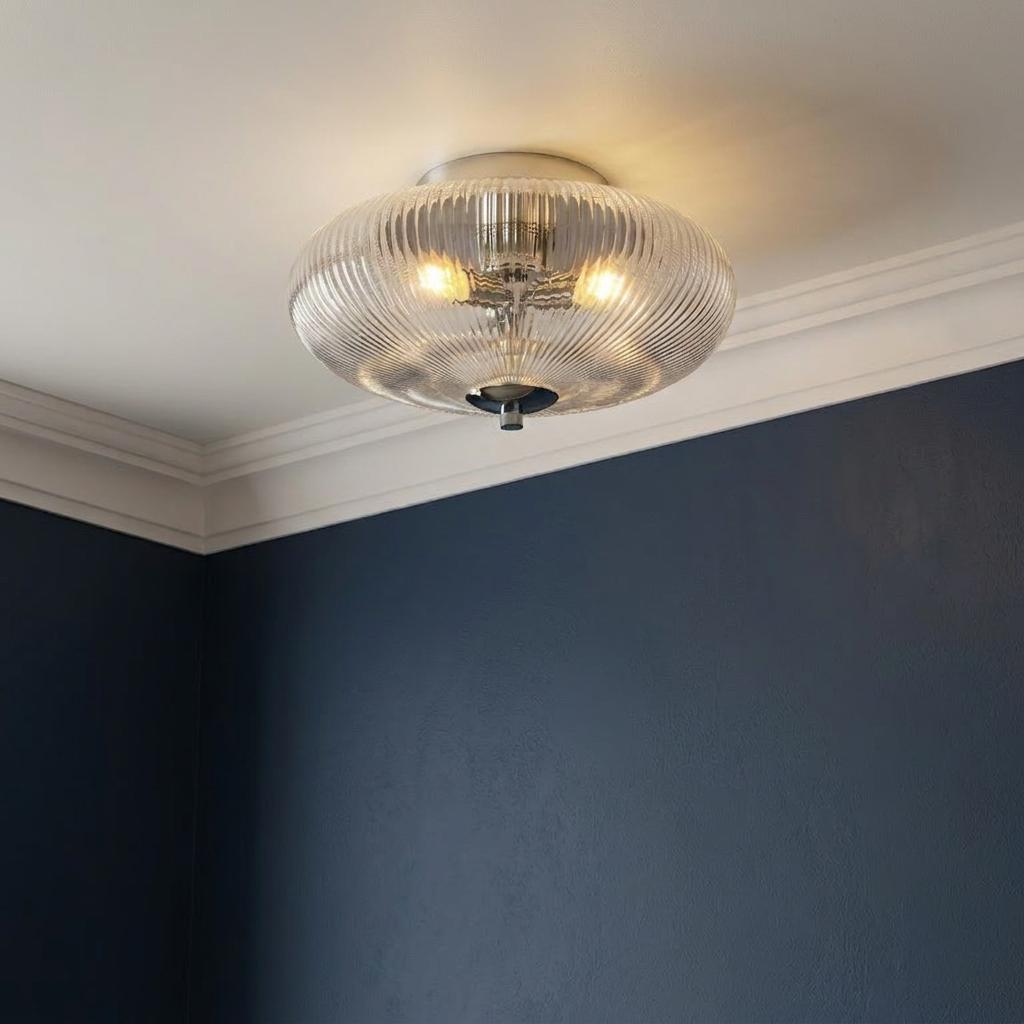 Ribbed glass flush ceiling light with chrome accents glowing on a white ceiling beside a navy blue wall.