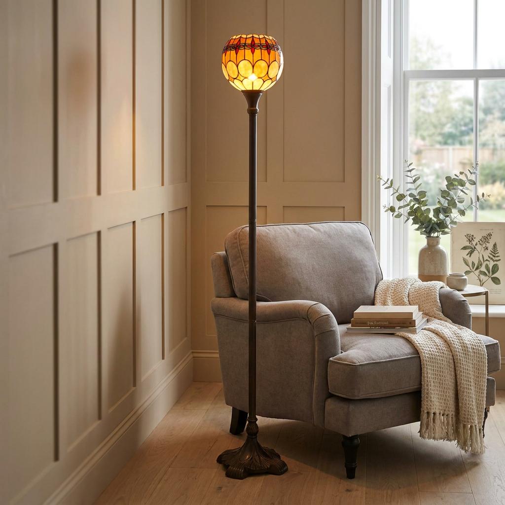 Atlantic Uplighter Tiffany Floor Lamp with an amber stained glass shade standing next to a grey armchair.
