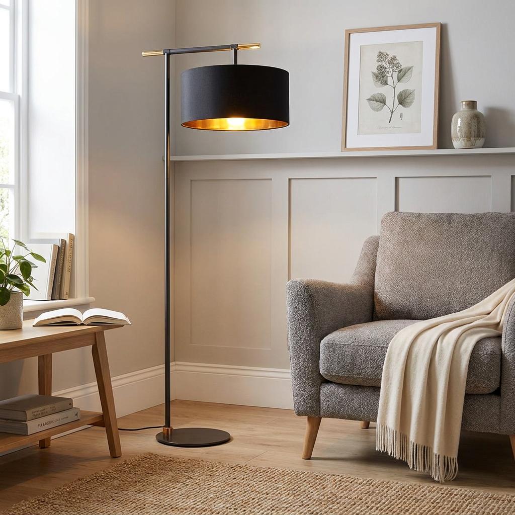 Modern black floor lamp with a gold interior shade illuminating a cozy living room next to a grey armchair.