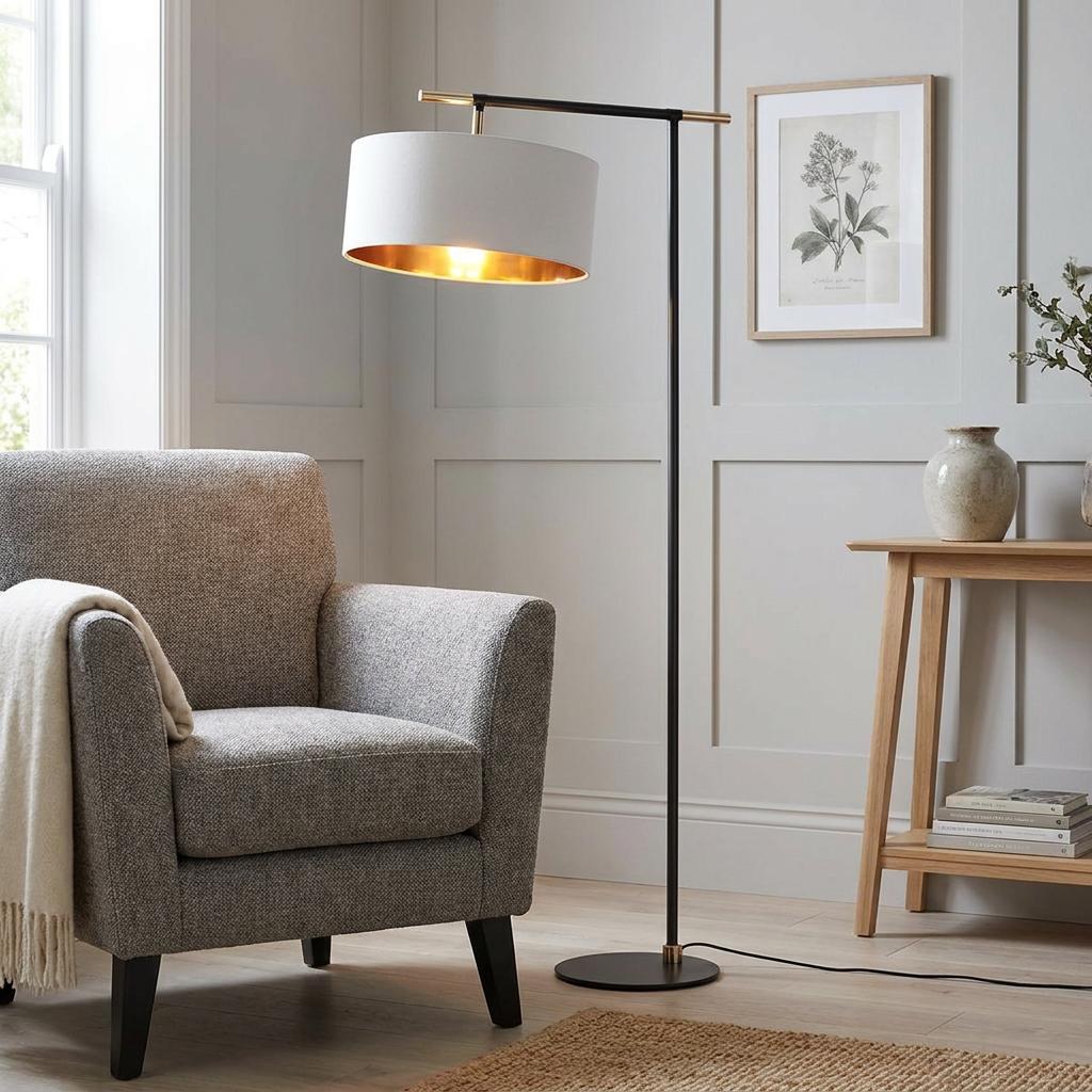 Balance 1 floor lamp with white drum shade and gold interior next to a grey armchair in a modern living room.