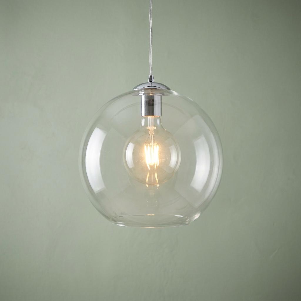 Clear glass globe pendant light with a lit filament bulb hanging against a soft green background.