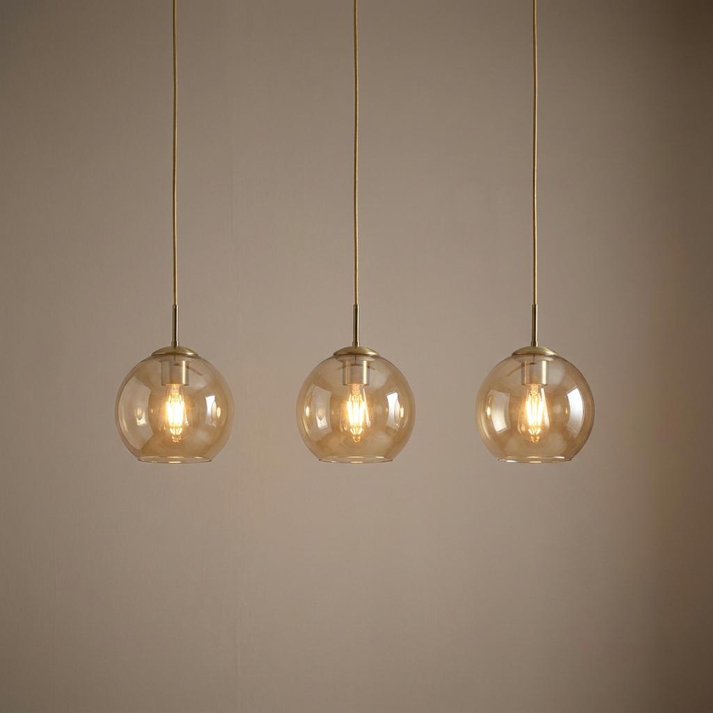 Trio of amber glass globe pendant lights with brass hardware hanging against a neutral wall.