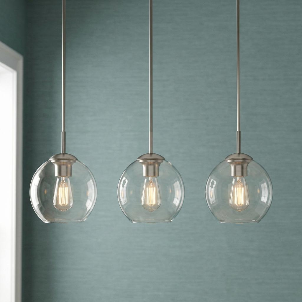 Three modern globe pendant lights with clear glass shades and glowing bulbs against a textured teal wall.
