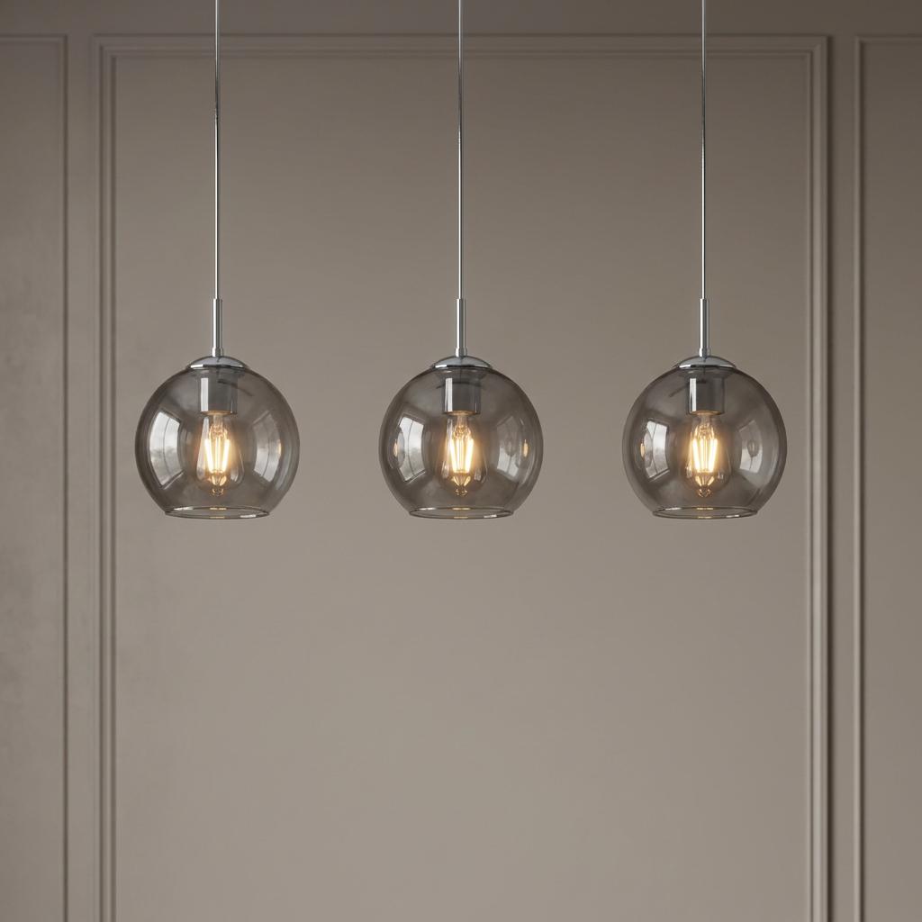 Three chrome pendant lights with smoked glass globe shades, illuminated against a neutral paneled wall.