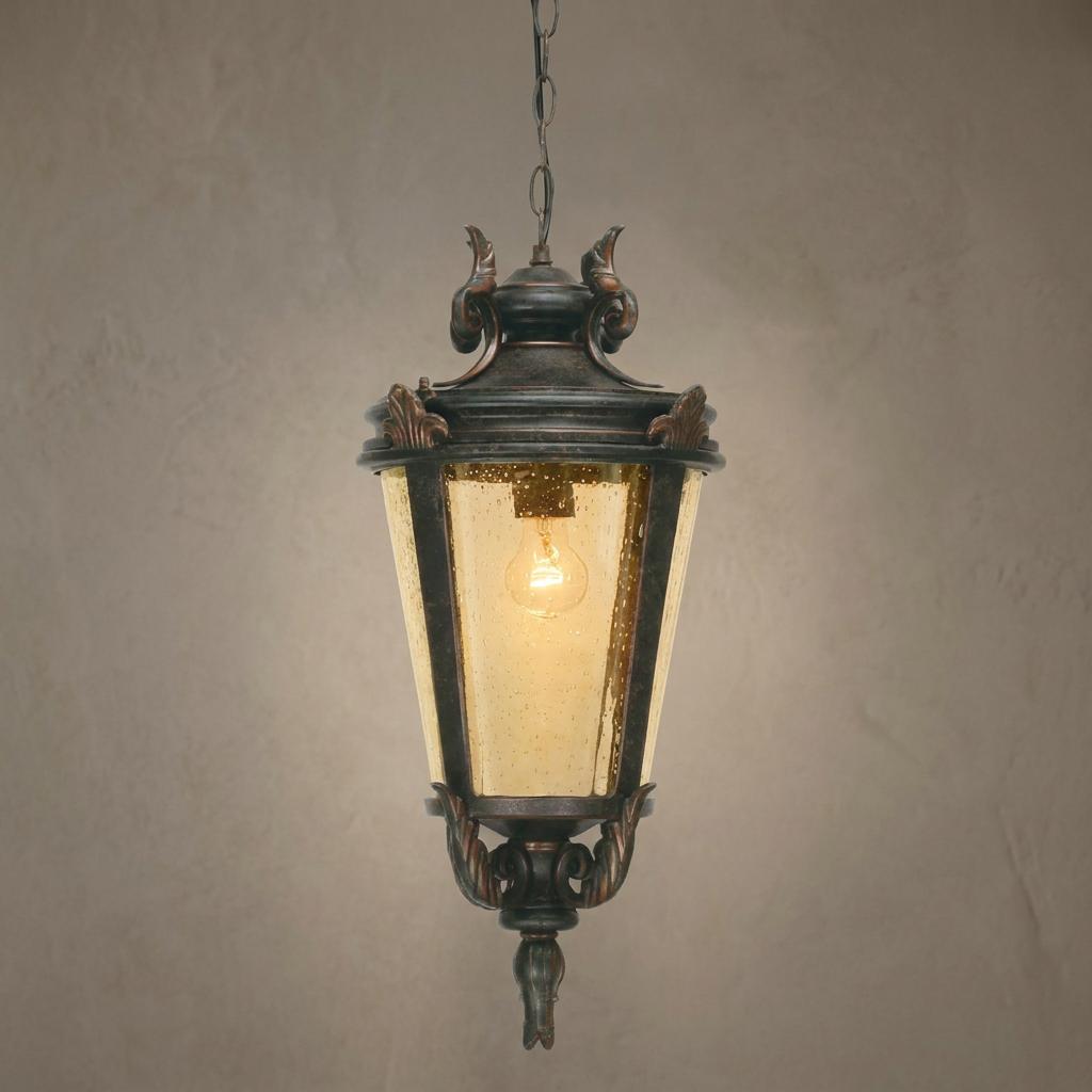 Ornate weathered bronze outdoor pendant light with amber seeded glass hanging against a textured wall.