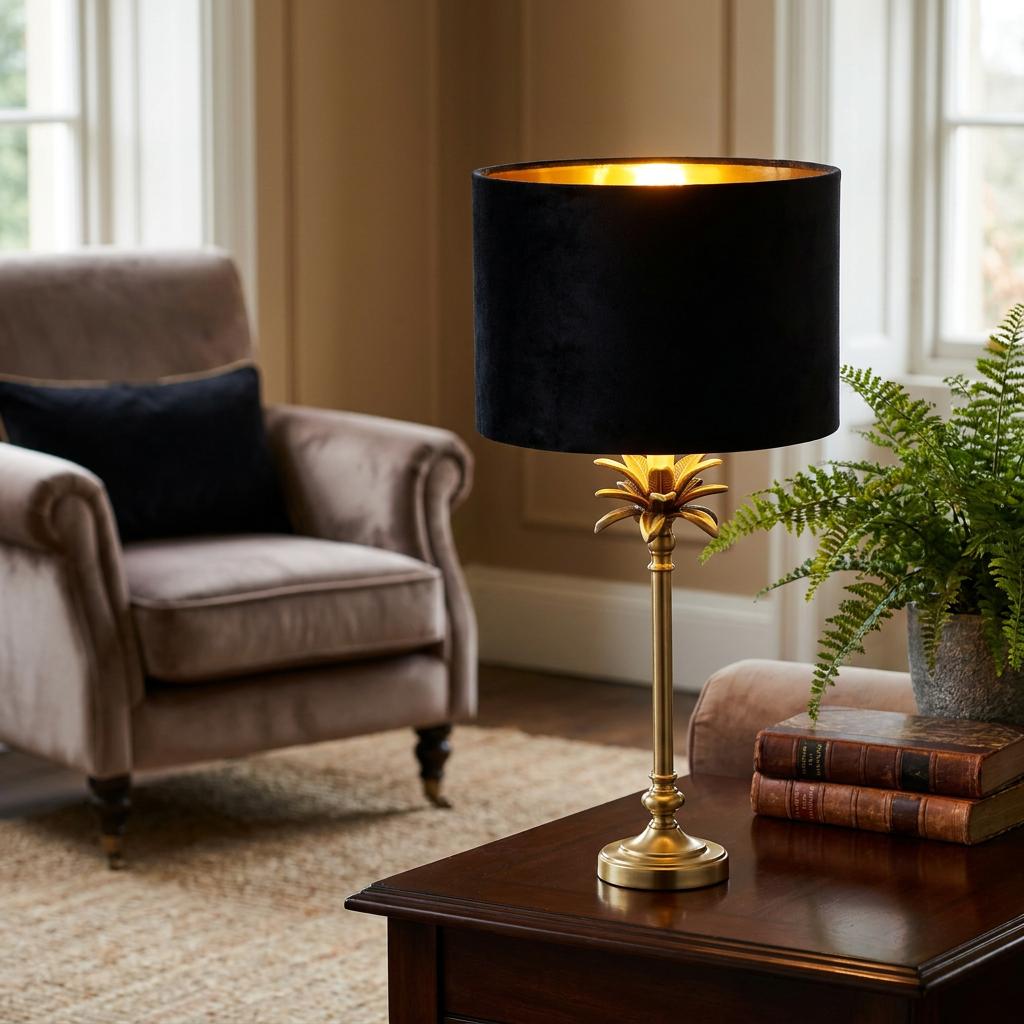 Satin brass palm table lamp with a black velvet shade on a wooden side table in a living room.