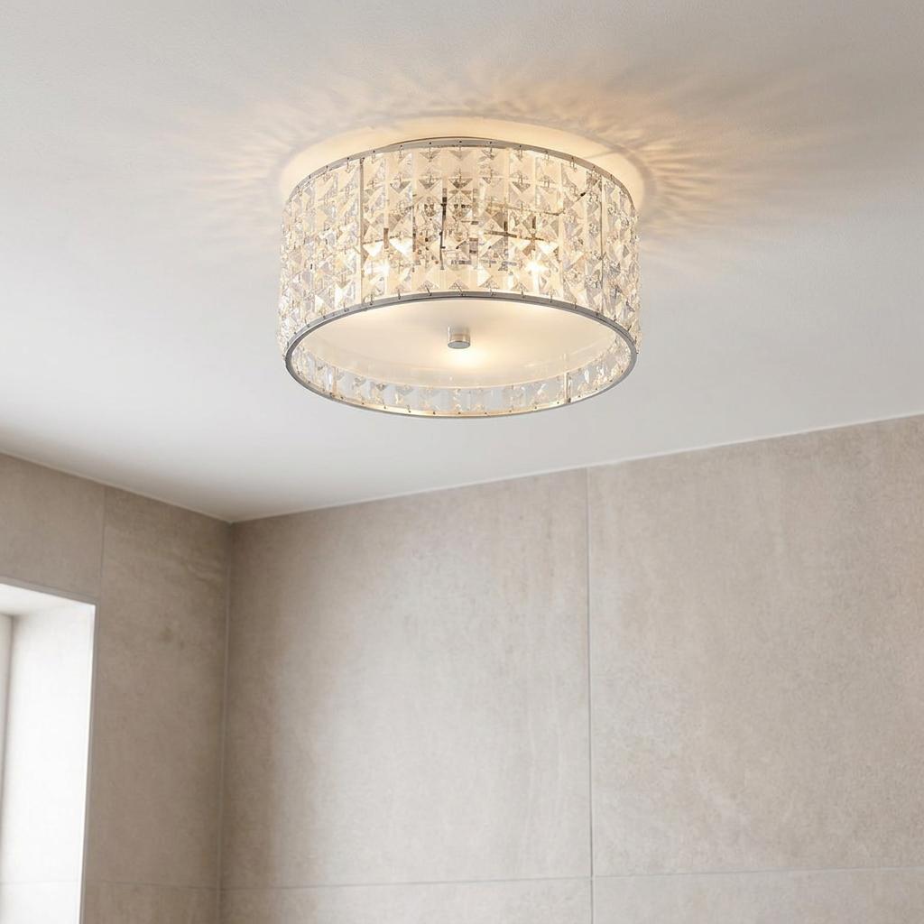 Crystal and chrome flush ceiling light glowing on a white ceiling above light grey bathroom tiles.