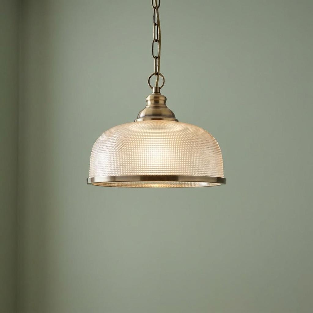 Brass pendant light with a textured glass dome shade and chain suspension against a light green wall.