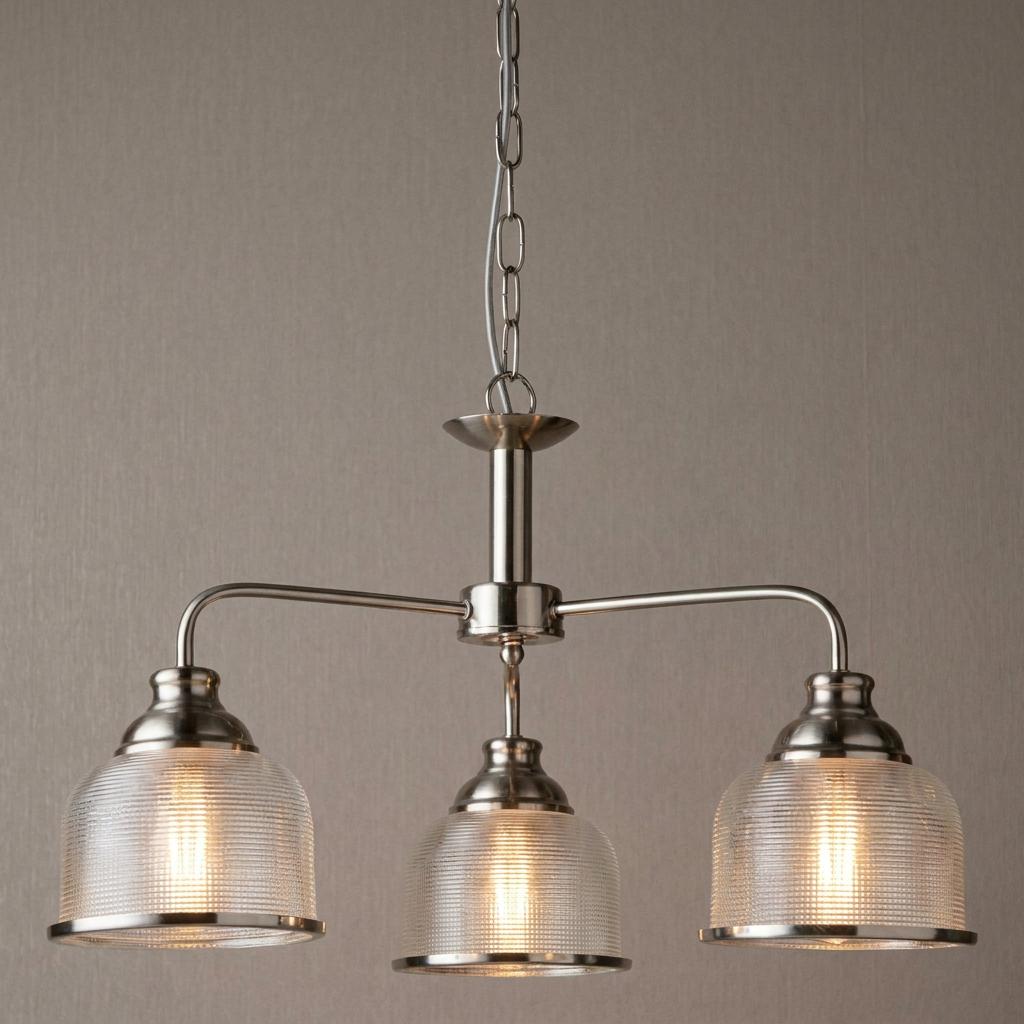 Three-light silver pendant chandelier with ribbed holophane glass shades against a textured wall.