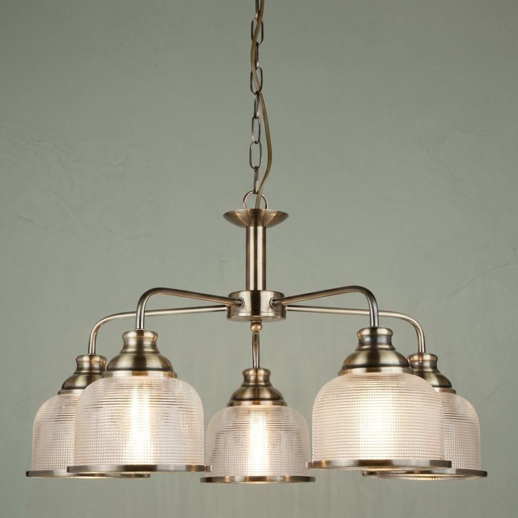 Five-light antique brass pendant chandelier with ribbed glass shades against a pale green wall.