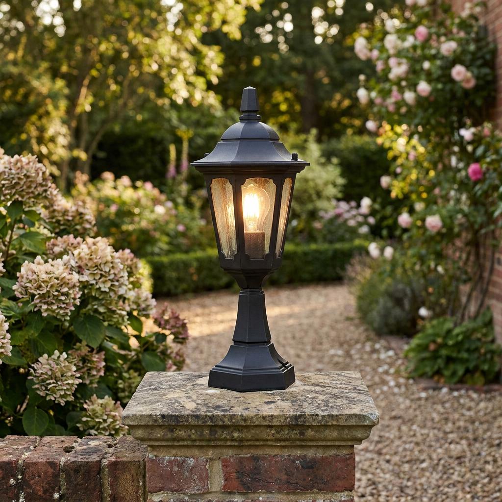 Black traditional outdoor lantern light mounted on a stone garden pillar with a glowing bulb.