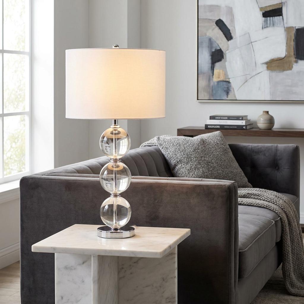 Lit table lamp with stacked glass spheres and white shade on a marble table in a modern living room.