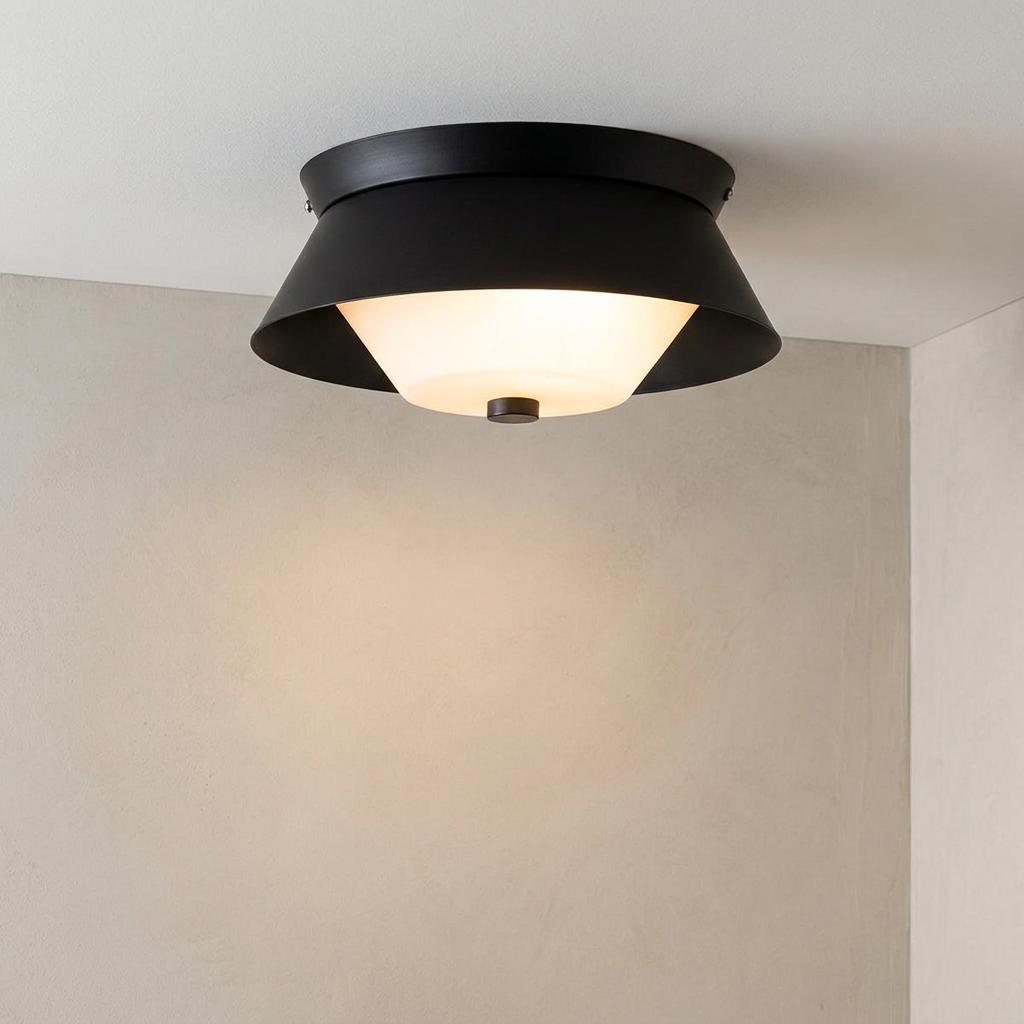 Modern black flush mount ceiling light with a frosted glass diffuser glowing against a neutral wall corner.