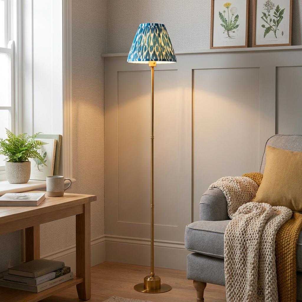 Brass floor lamp with a blue ikat shade stands next to a grey armchair in a cozy, sunlit living room.