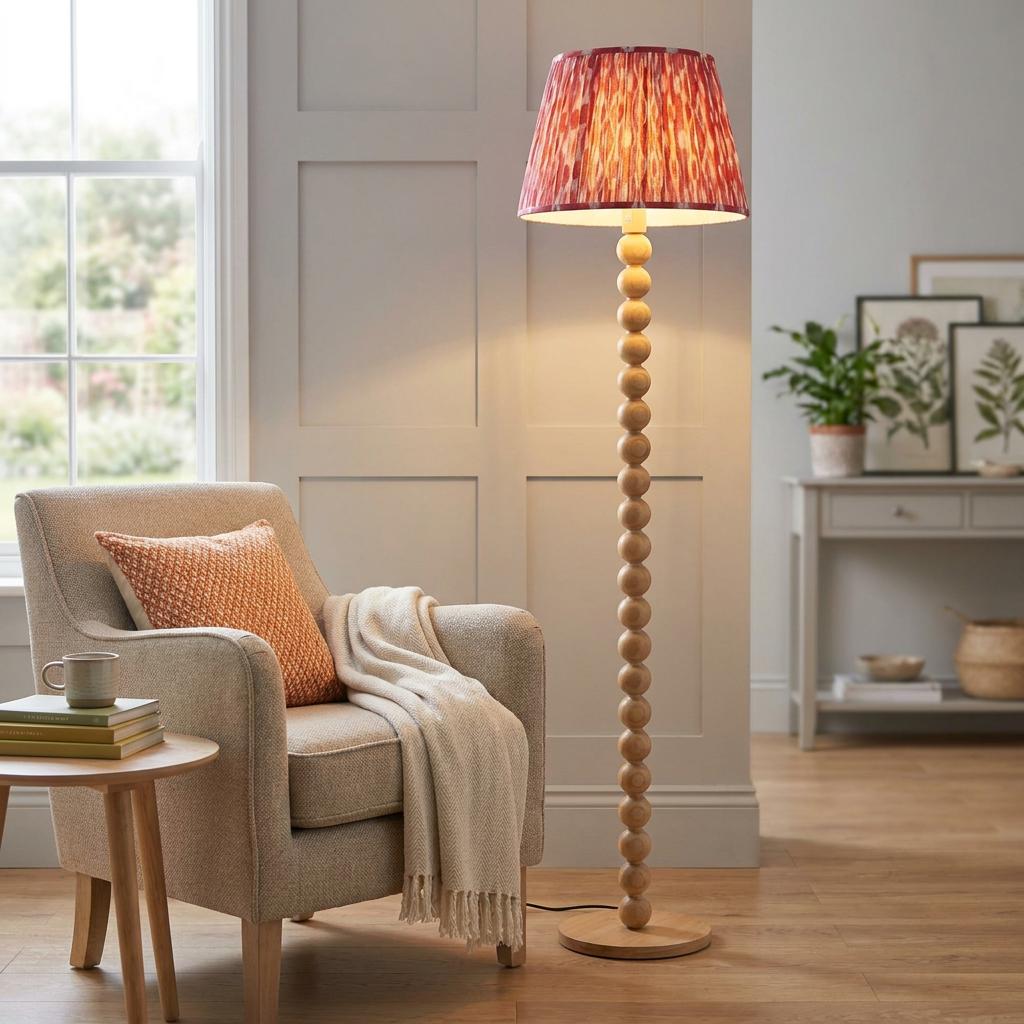 Cane bamboo floor lamp with a coral pink ikat shade stands next to a neutral armchair in a cozy living room.