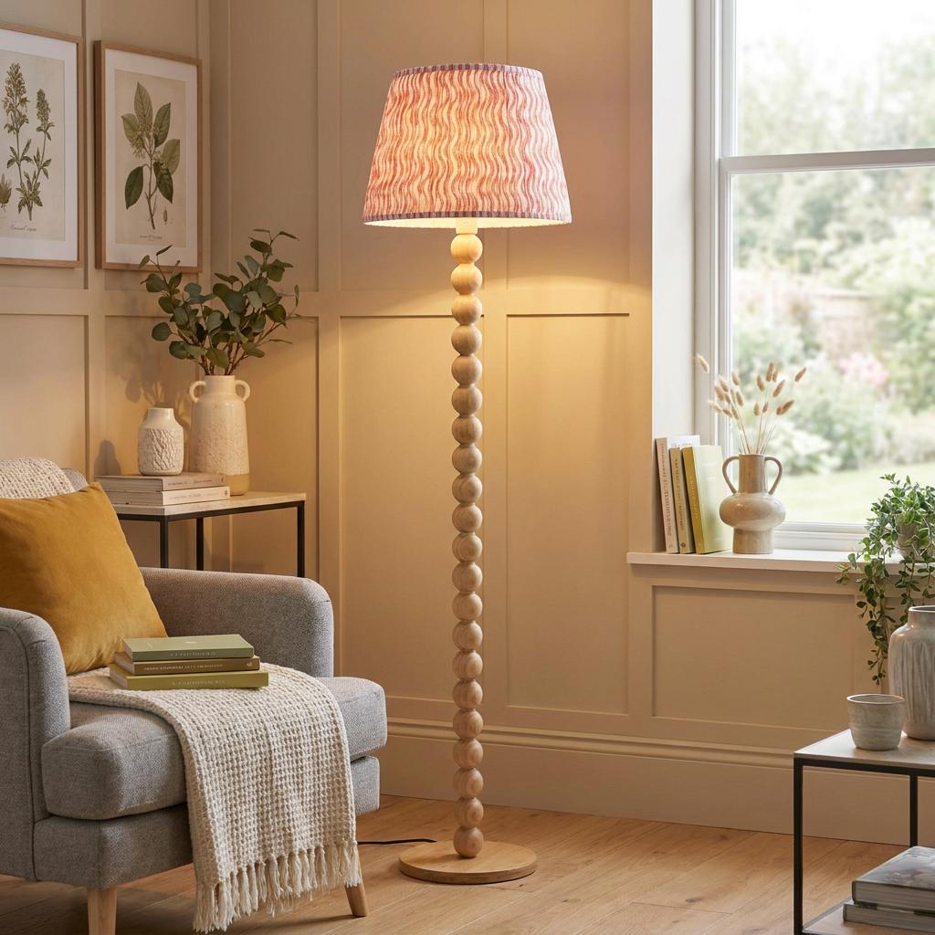 Cane bamboo floor lamp with a coral pink ripple shade in a cozy living room setting next to a grey armchair.