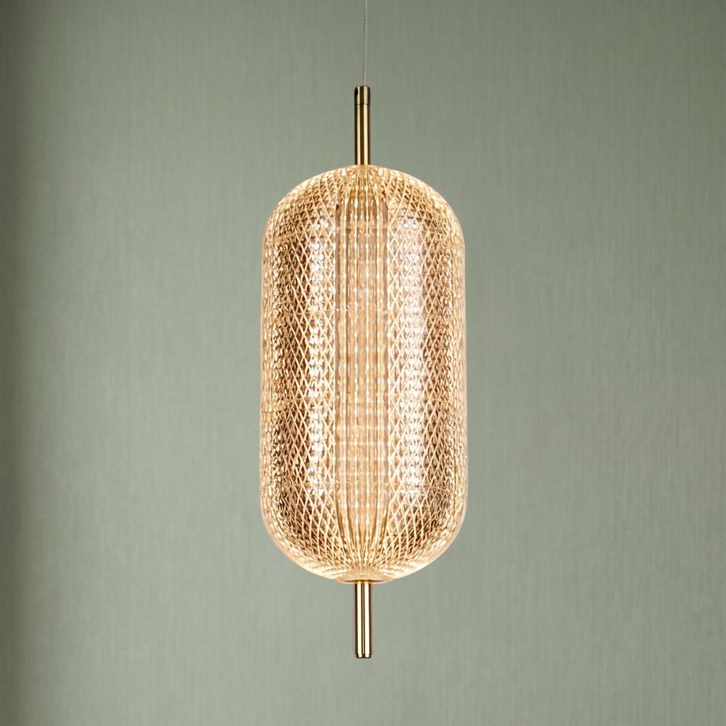 Capsule-shaped pendant light with textured glass and satin brass accents glowing against a sage green background.