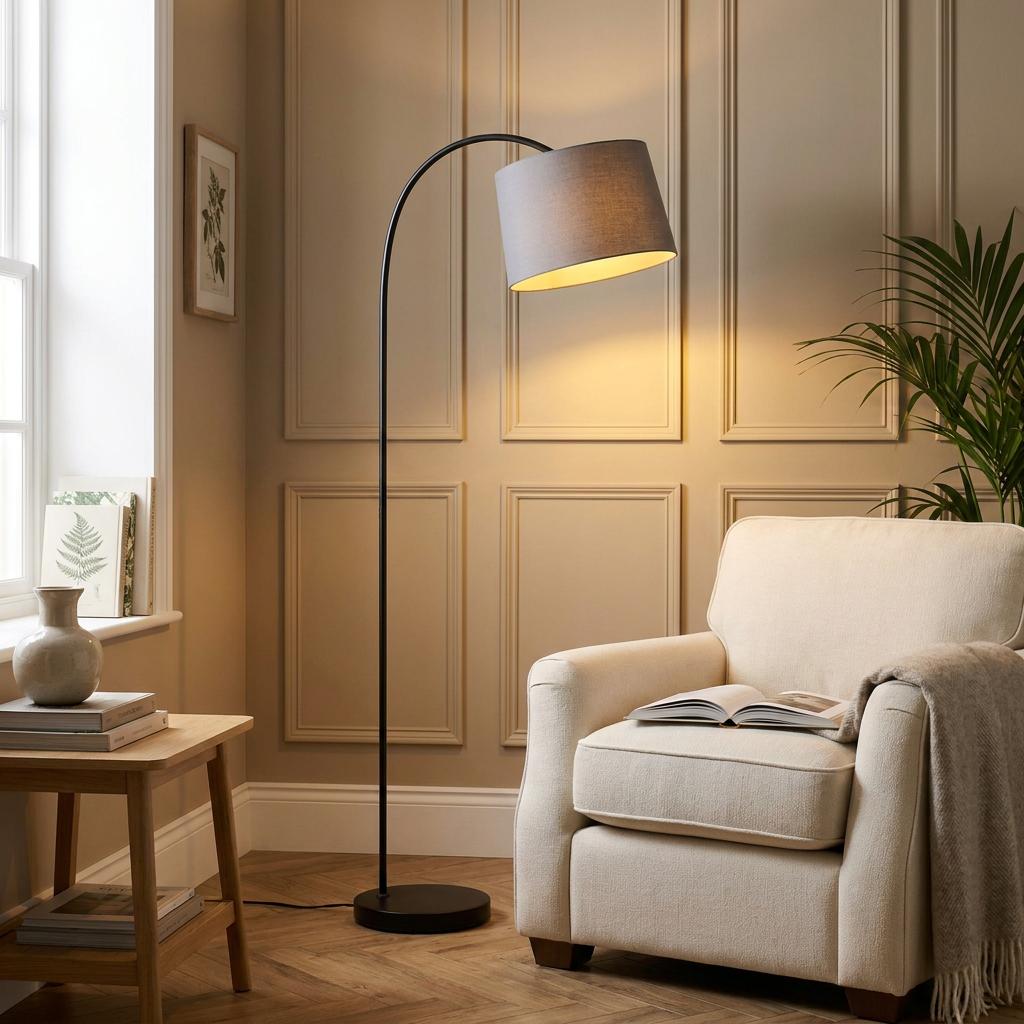 Black arched floor lamp with a grey fabric shade standing next to a cream armchair in a neutral living room.
