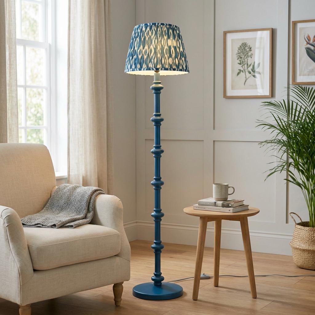 Blue spindle floor lamp with a patterned ikat shade in a bright living room by an armchair and side table.