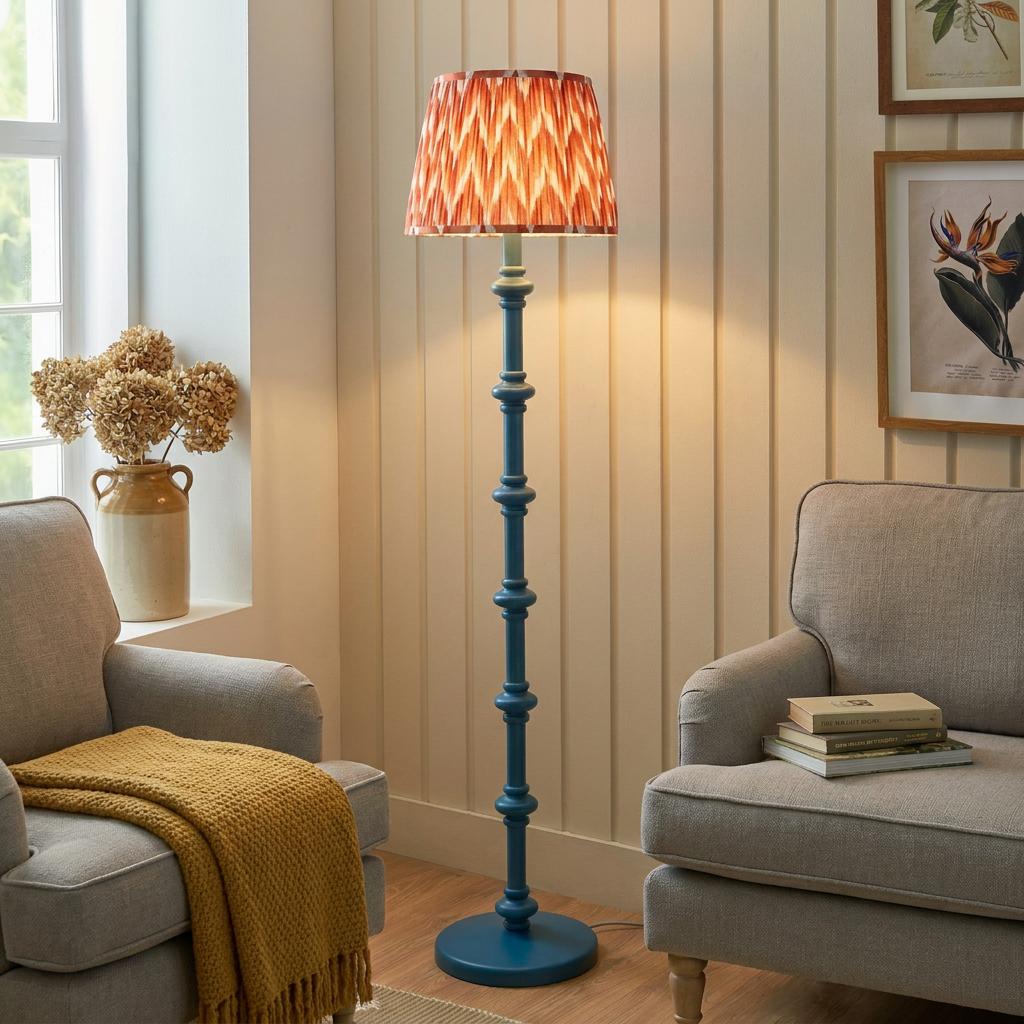 A teal bobbin floor lamp with an orange zigzag shade stands between two grey armchairs in a cozy living room.