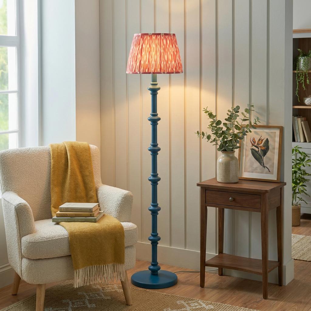 Carnaby blue floor lamp with a coral pink Ikat shade next to a cream armchair in a warmly lit living room.
