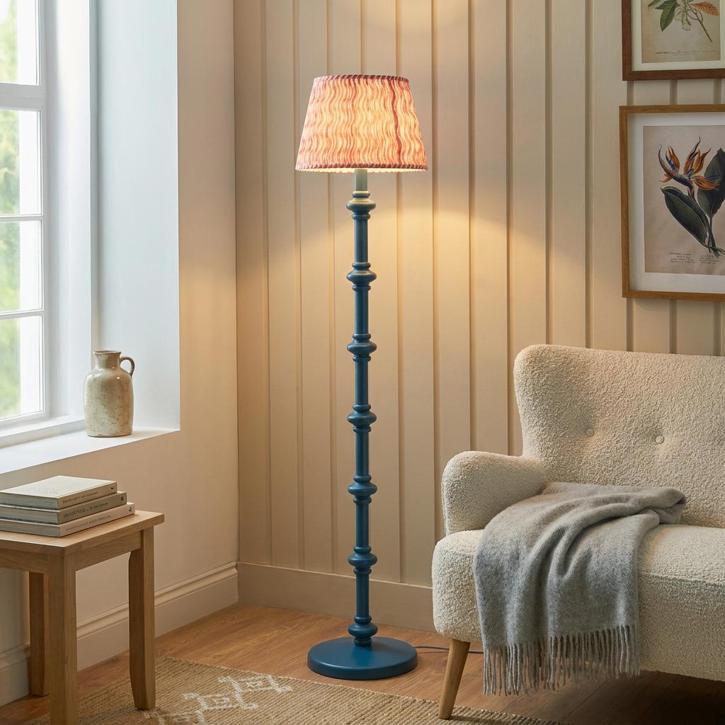 Carnaby blue floor lamp with a coral pink ripple shade lit in a living room beside a white armchair.