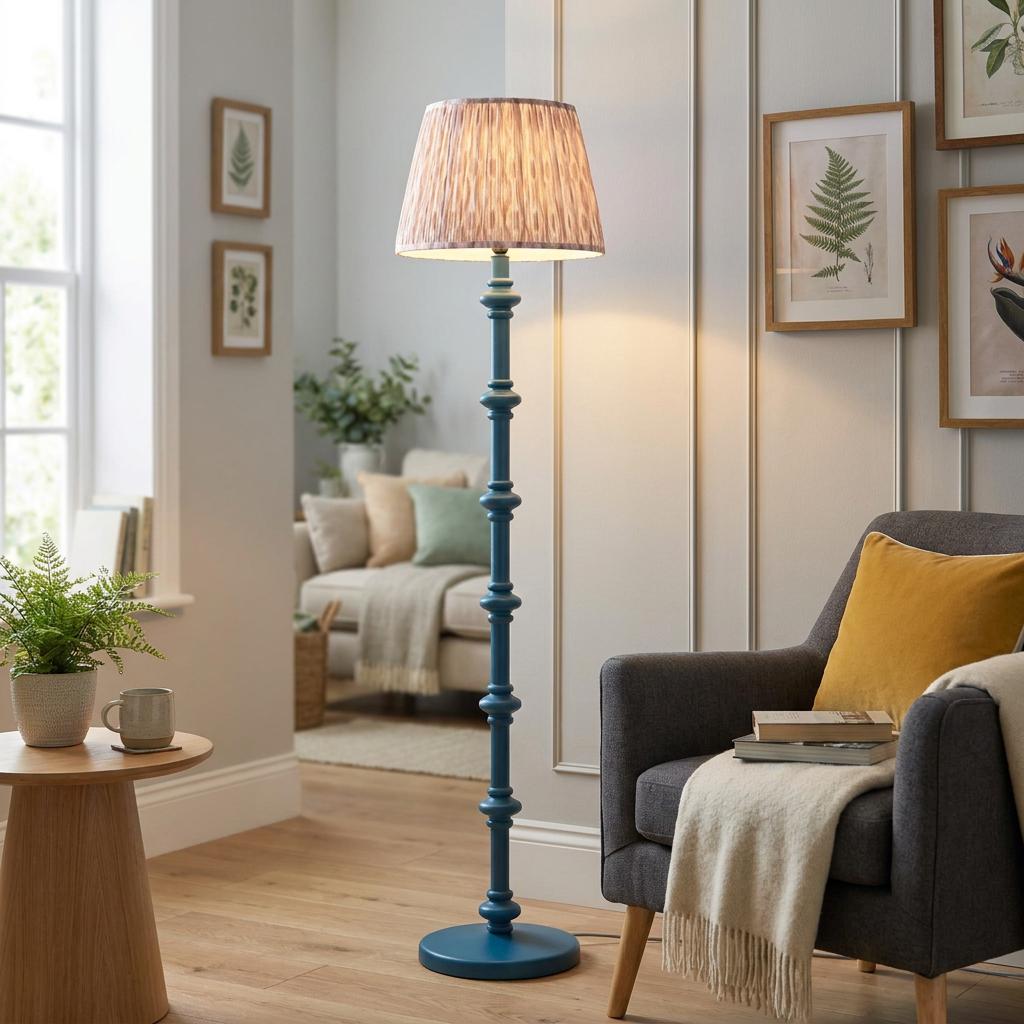 Blue spindle wooden floor lamp with an ikat neutral shade stands next to a grey armchair in a cozy living room.