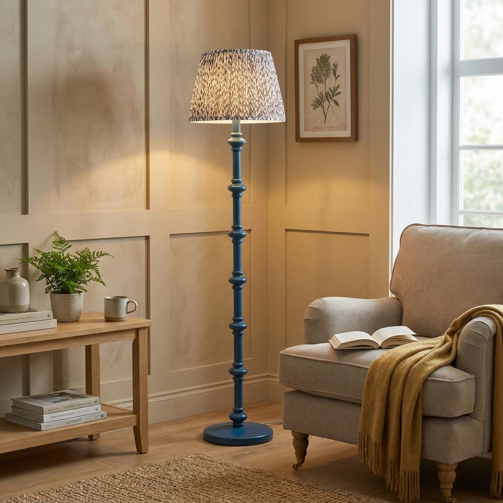 Blue turned wood floor lamp with a leaf print shade stands in a cozy living room next to a beige armchair.