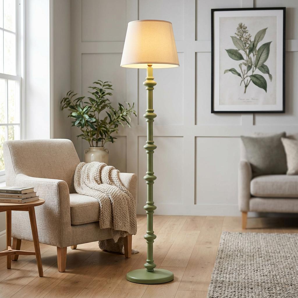 Green spindle floor lamp with a vintage white shade in a neutral-toned living room with an armchair.