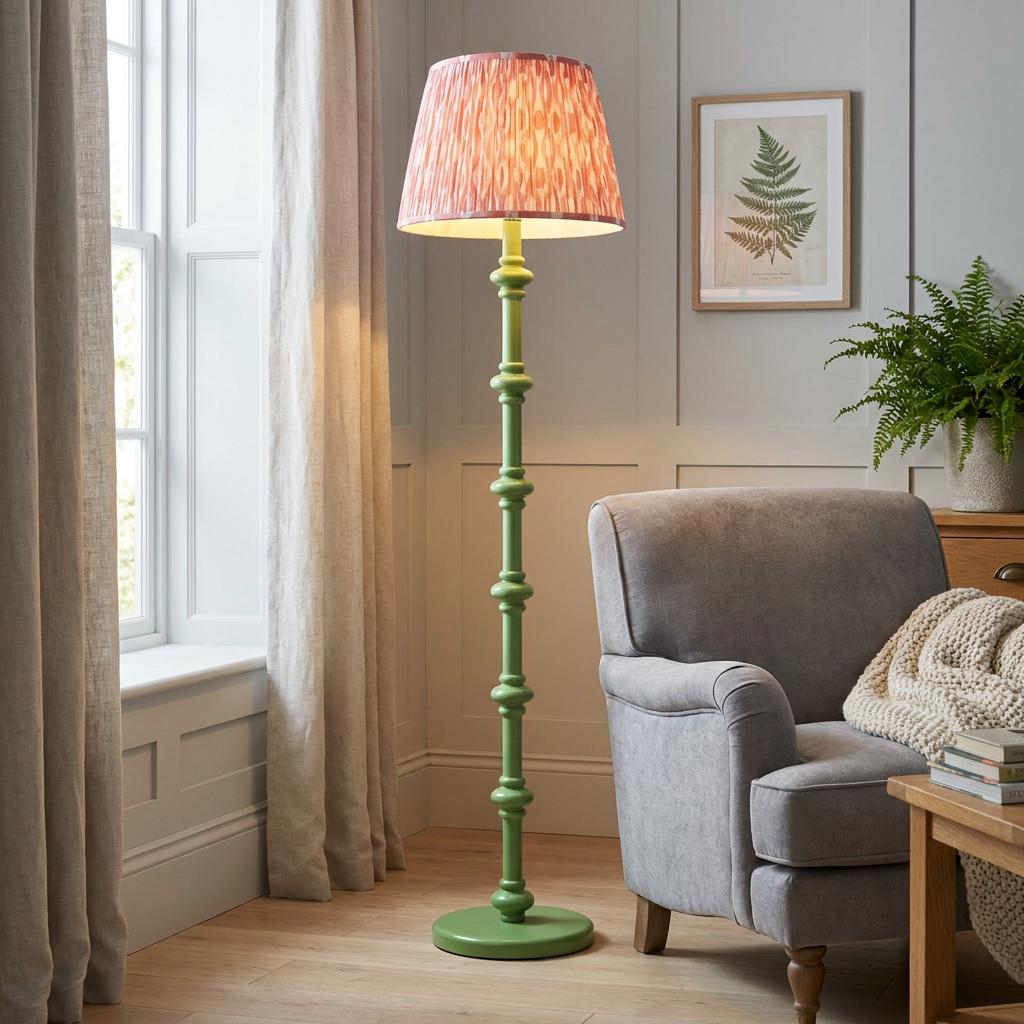 Green wooden floor lamp with a coral pink Ikat shade in a living room next to a grey armchair.