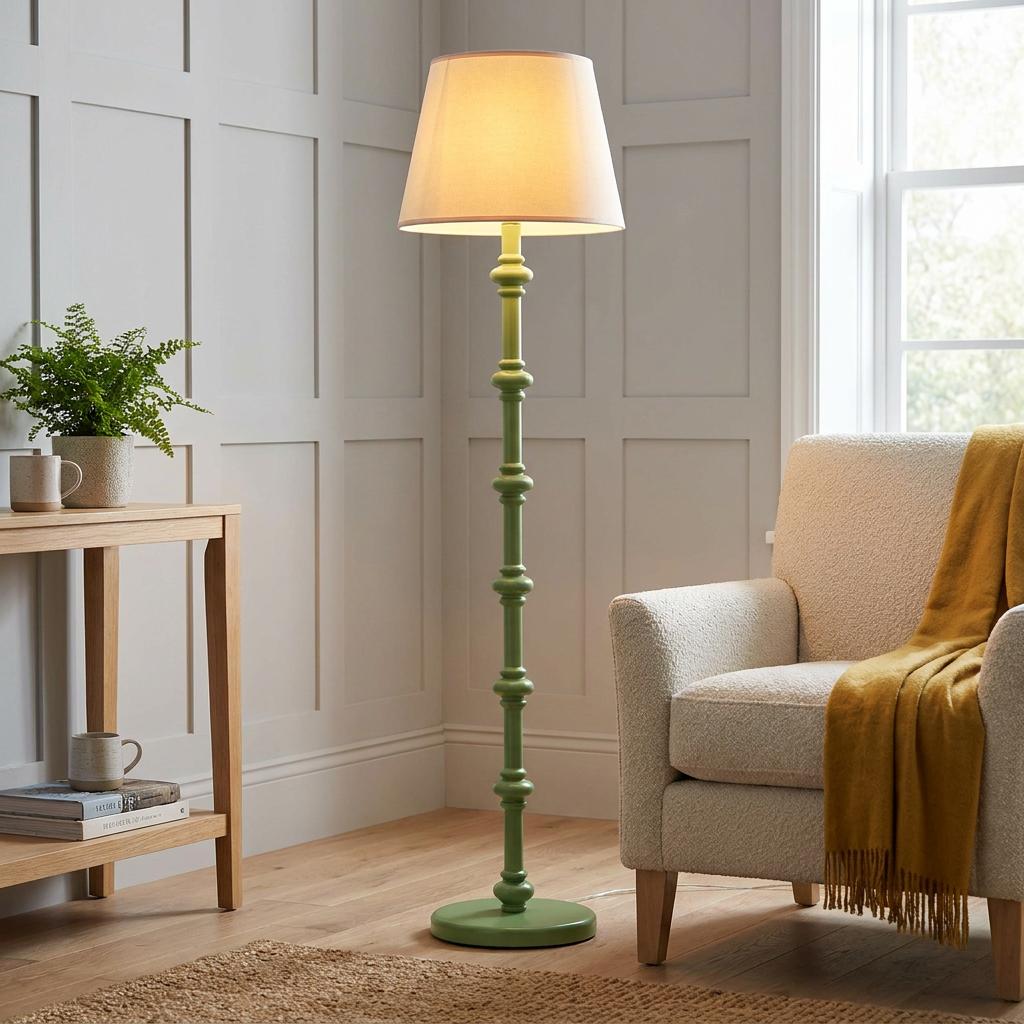 Carnaby green spindle floor lamp with a vintage white shade standing next to a cream armchair in a living room.