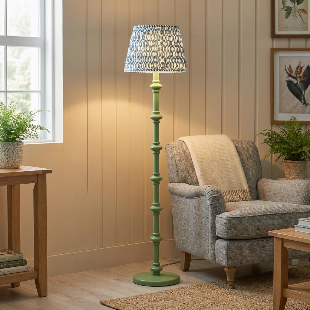 Green wooden floor lamp with a blue ripple shade stands beside a grey armchair in a cozy, neutral living room.