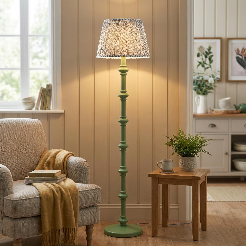 Green spindle floor lamp with a grey leaf pattern shade in a cozy living room with an armchair.