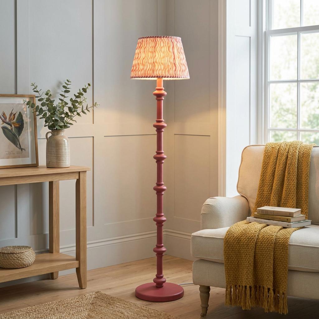 Pink spindle floor lamp with a patterned coral shade illuminated in a cozy living room next to an armchair.