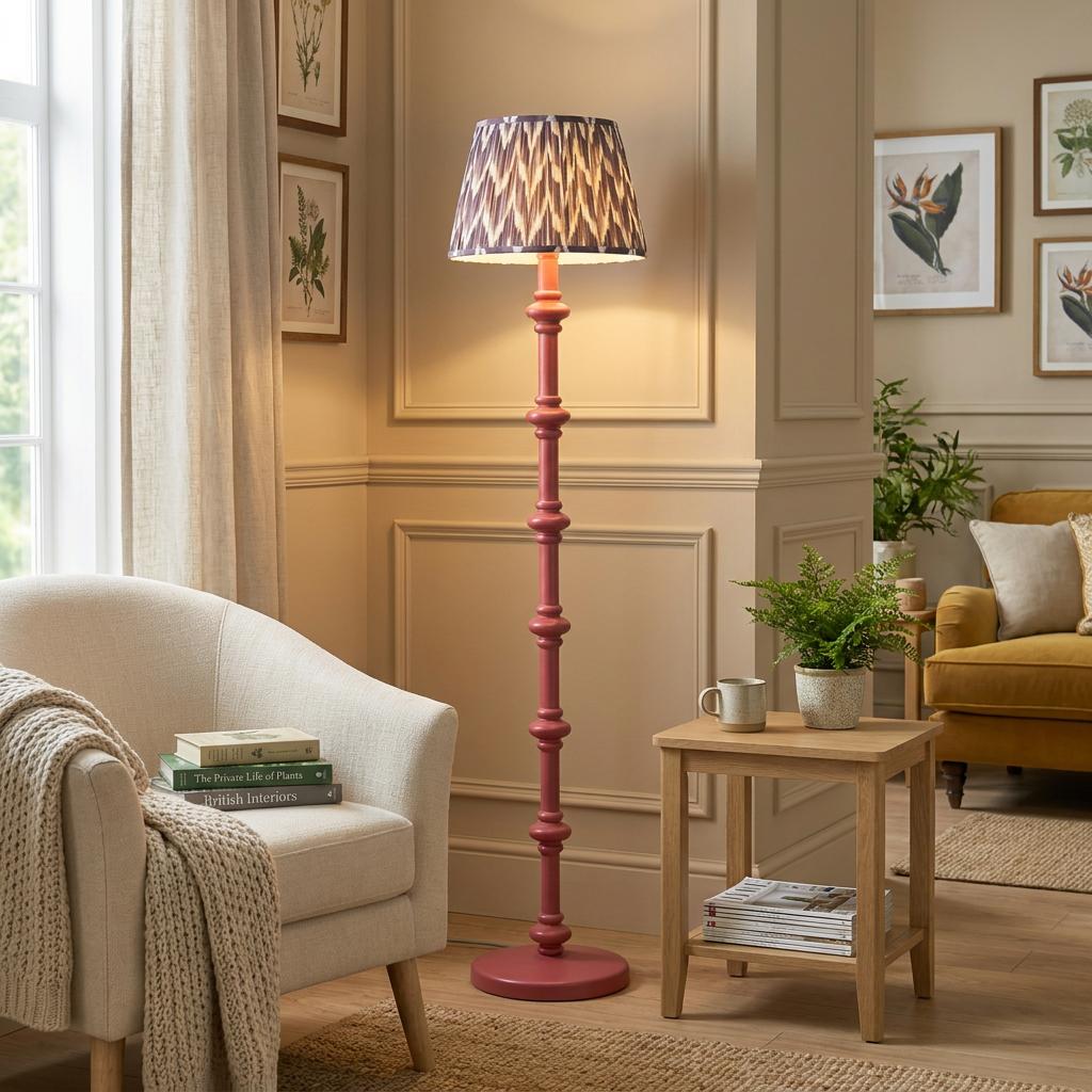 Pink spindle floor lamp with a grey zigzag shade in a neutral-toned living room beside a white armchair.