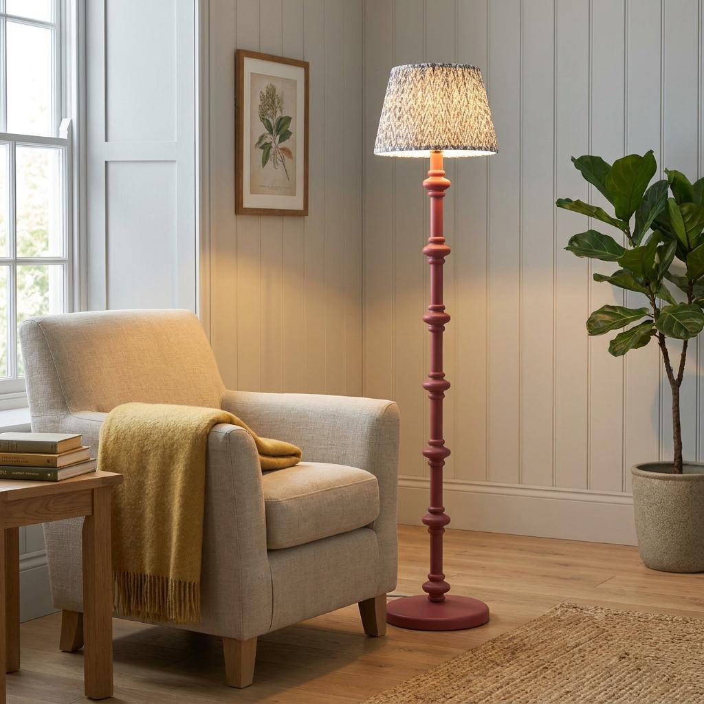 Pink floor lamp with a leaf-patterned shade beside a beige armchair with a yellow throw in a bright living room.