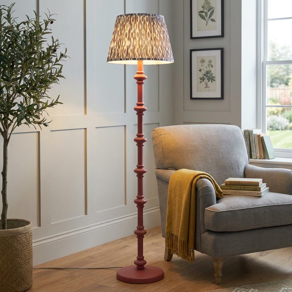 Pink turned wooden floor lamp with a grey ikat shade next to a grey armchair in a cozy paneled living room.