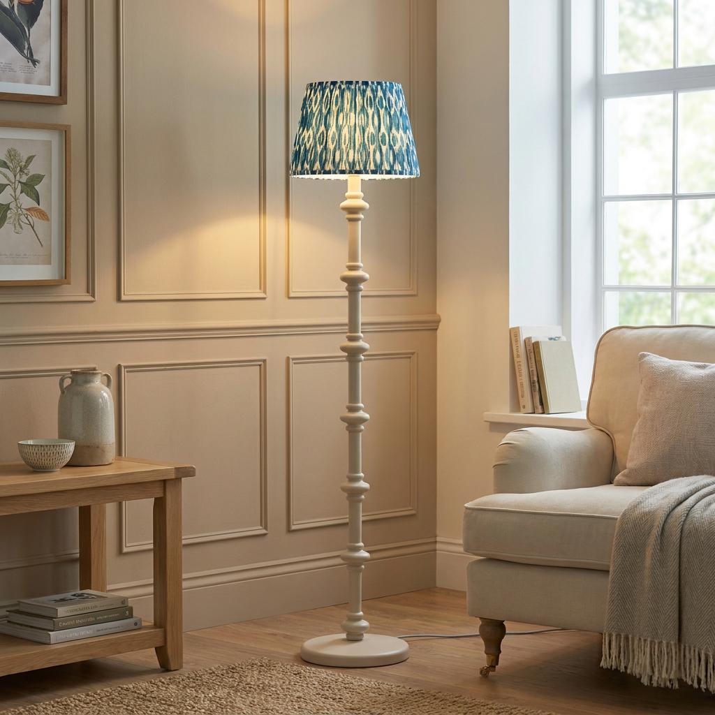 White bobbin floor lamp with a blue ikat pattern shade standing in a neutral paneled living room.