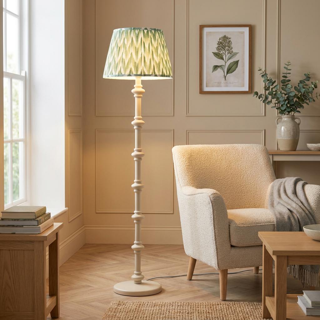 White wooden floor lamp with a green zigzag shade standing next to a cream armchair in a living room.