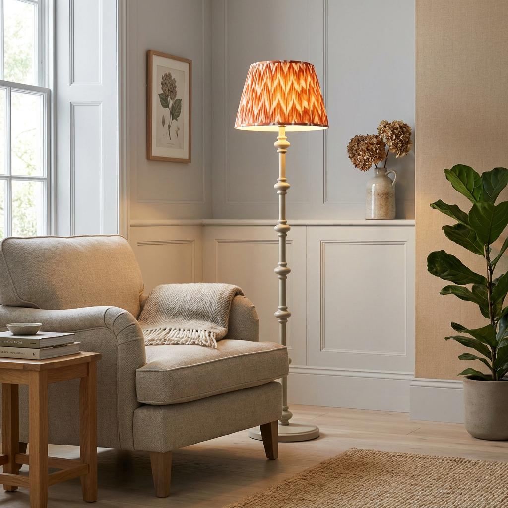 White wooden floor lamp with an orange zigzag shade beside a cozy beige armchair in a paneled living room.