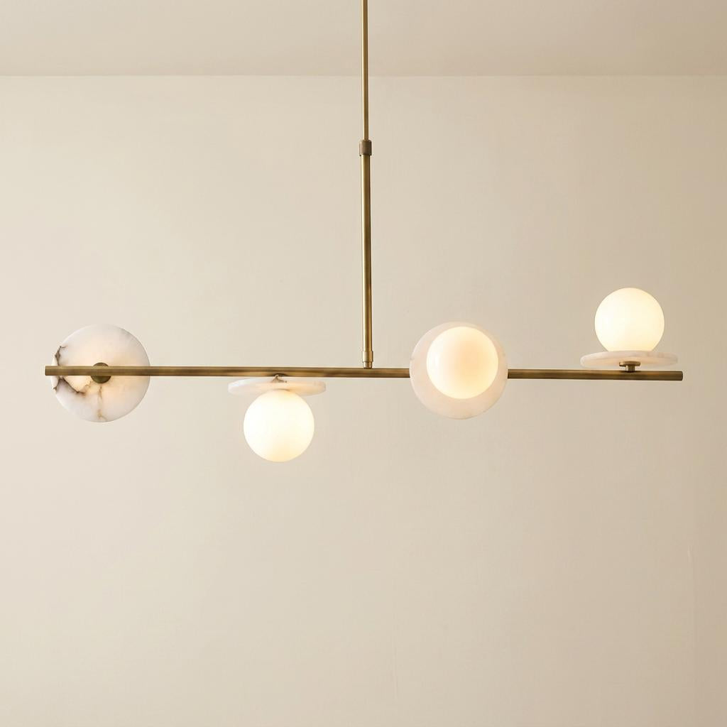 Cerchio linear brass pendant light with four opal glass globes and marble accents against a neutral wall.