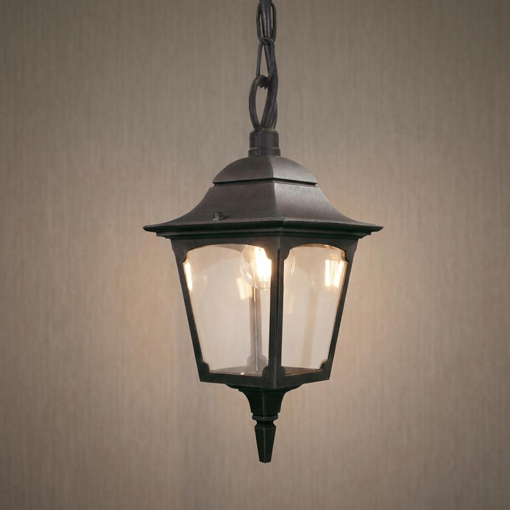 Chapel 1 Light black chain outdoor lantern with a lit bulb against a textured wall.