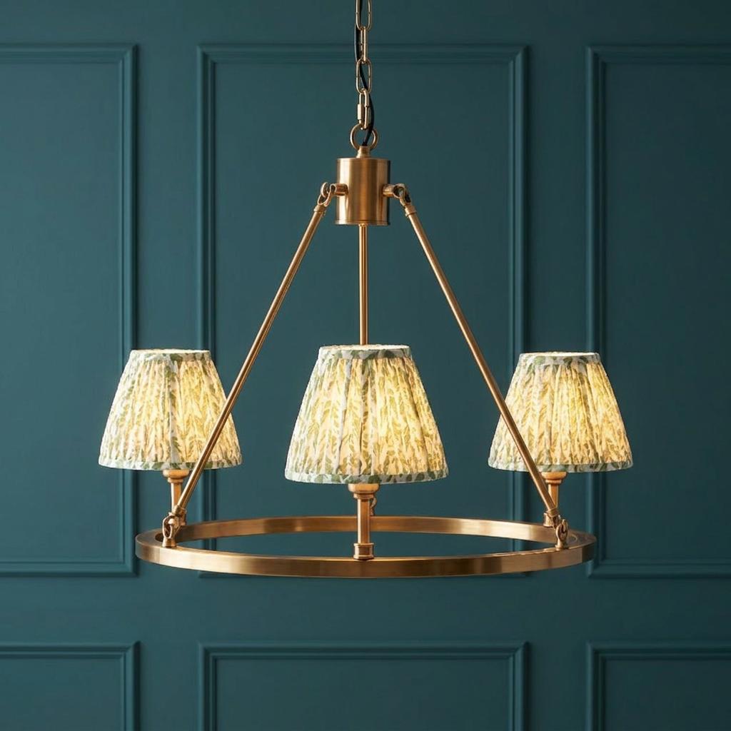 Brass hoop chandelier with three green leaf print shades against a teal paneled wall.