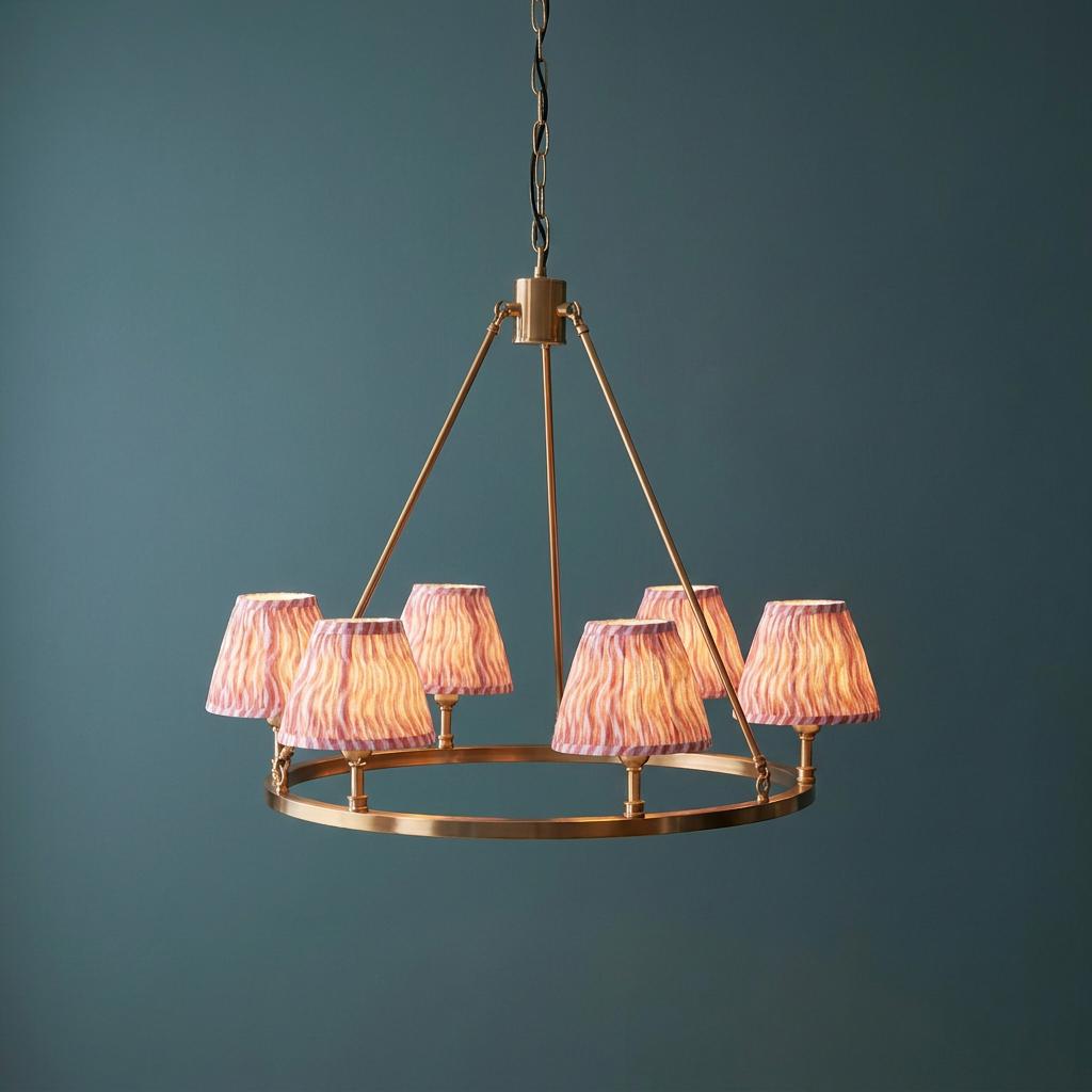 Large brass circular pendant light with six pink ripple fabric shades hanging against a dark teal wall.